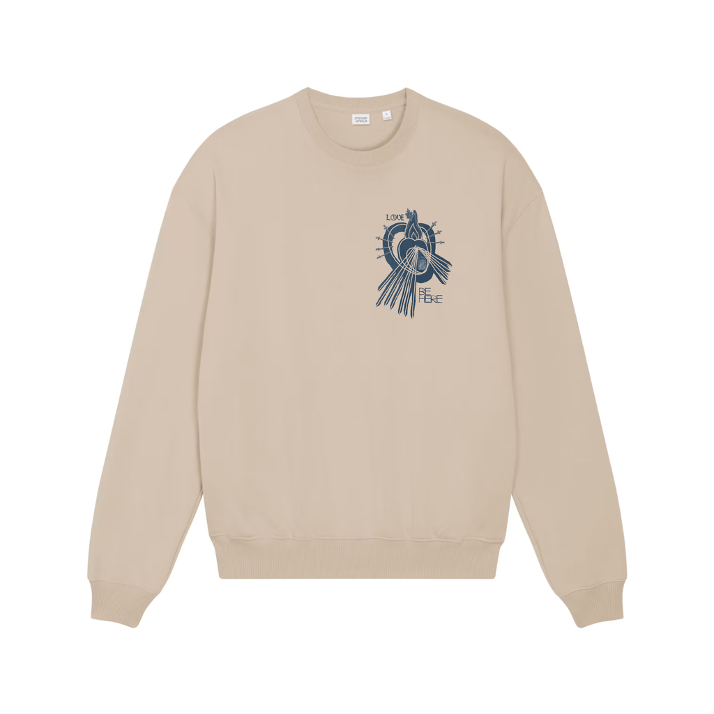 A beige crewneck sweatshirt shown from the front, featuring an indigo blue graphic print of a little human heart enclosed in the womb of the Sacred Divine Mercy Heart of Jesus enclosed in the womb of Immaculate Sorrowful Heart of Mary with the words LOVE and BE HERE